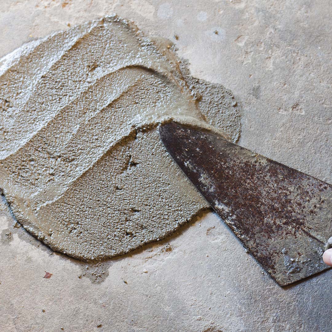 Hand using trowel with wet concrete floor.
